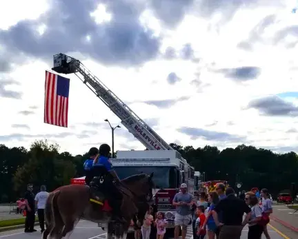 Two police officers on horses, talking to a group of parents and kids. They are all outside and in front of a fire truck.