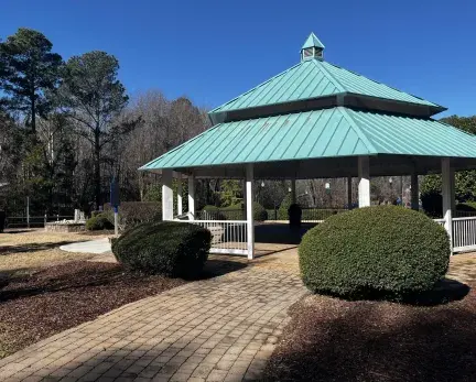 Teal gazebo with white railing and green circular bushes around.