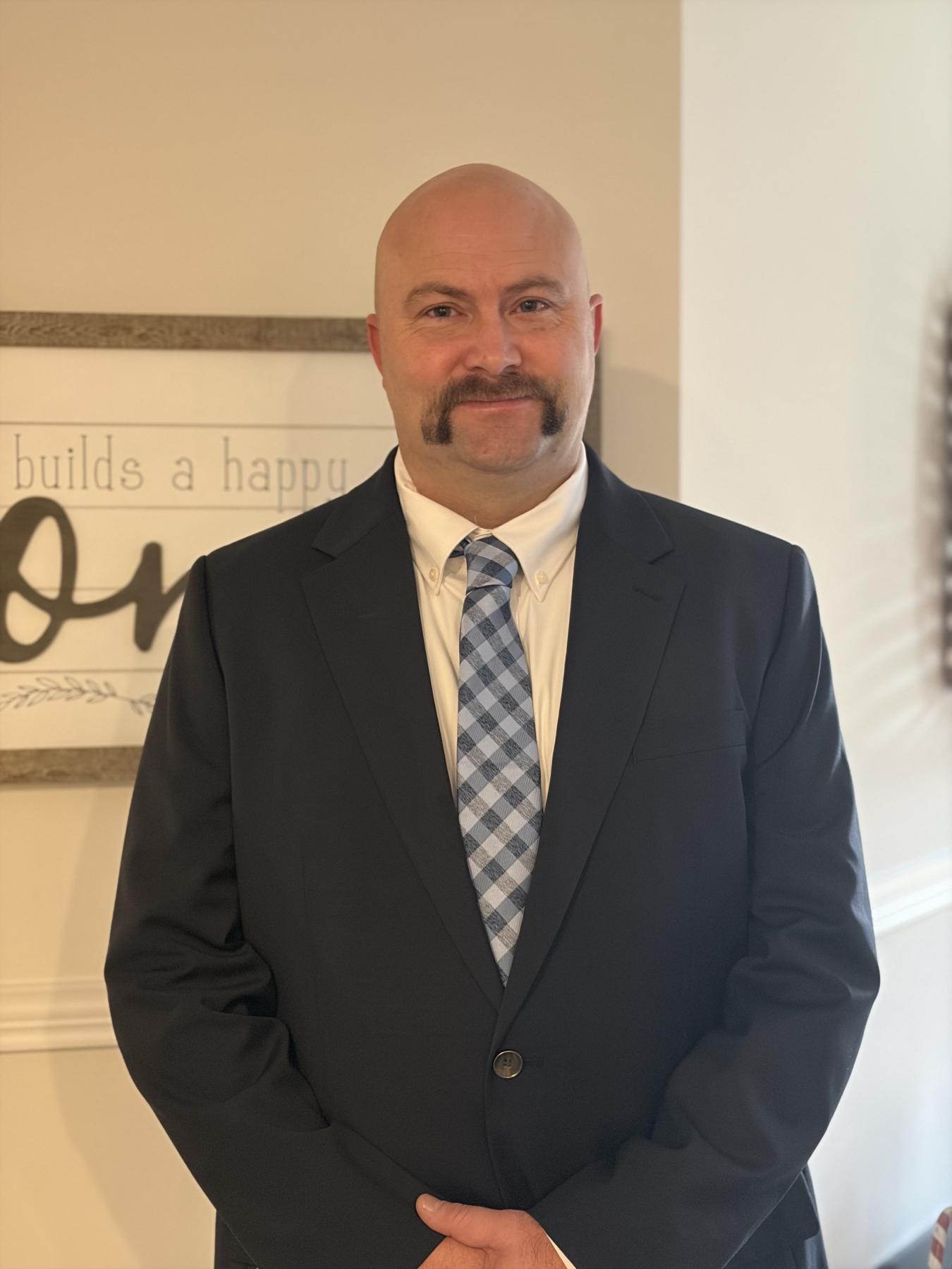 Man in blue suite with light blue tie standing by a wall
