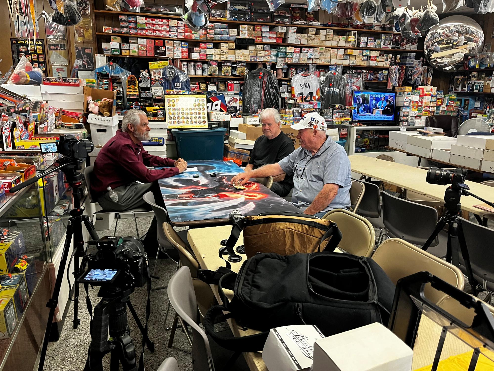 Mayor sitting with two men at baseball card shop.