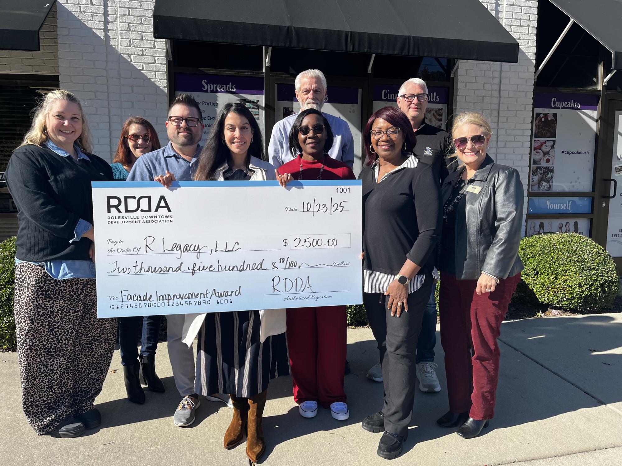 People standing in front of large white building when check of $2500.