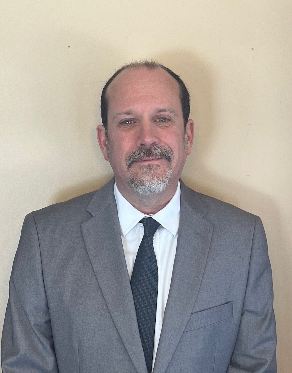 Man in a grey suit and black tie with a white shirt.