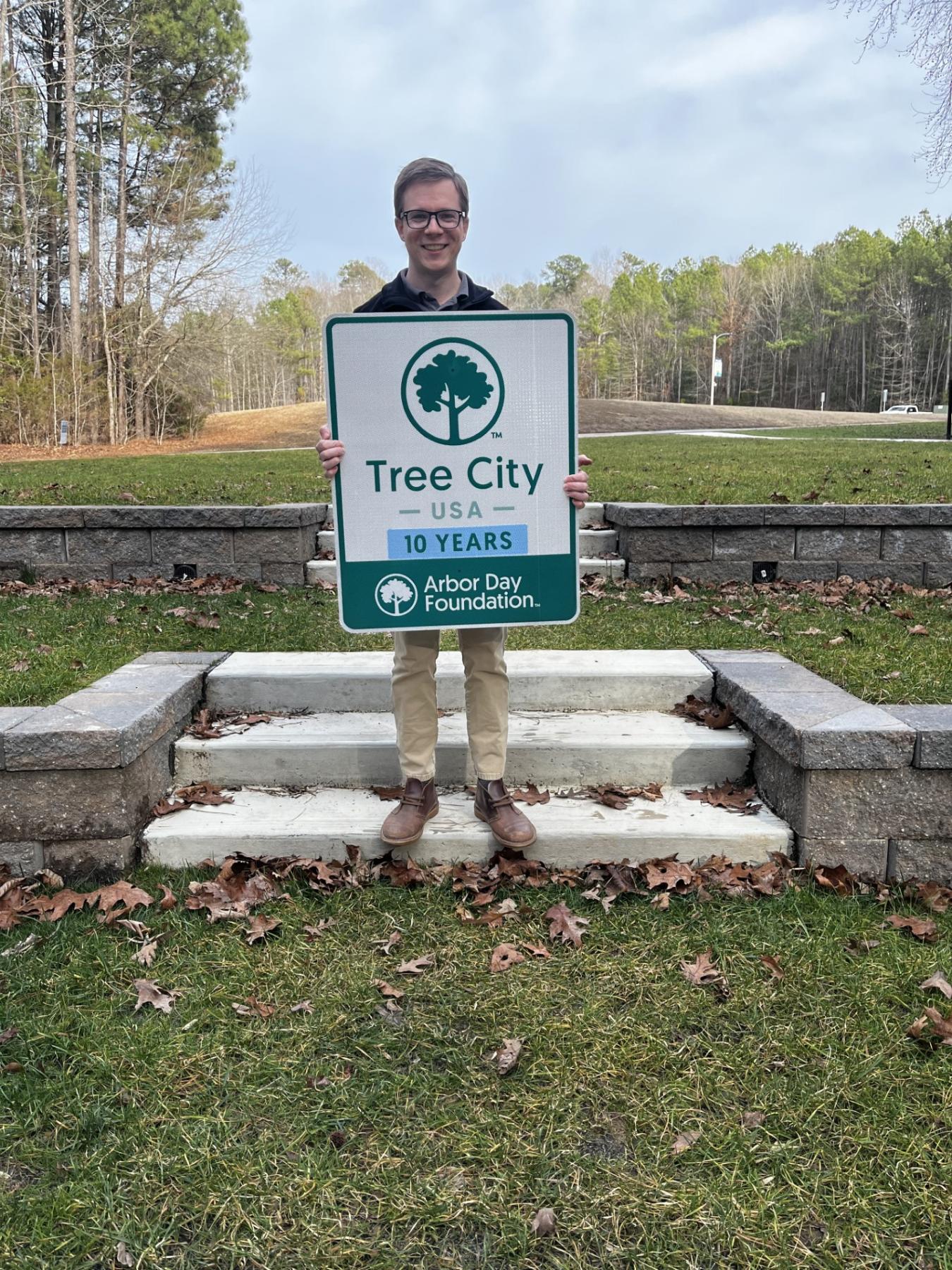 Town Staff member standing at Mill Bridge Nature Park Amphitheater with Tree City USA sign
